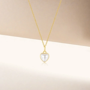 Détail d'un pendentif cœur en perle sur une chaîne dorée au design élégant et épuré