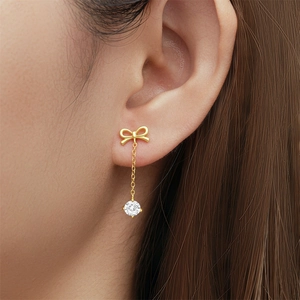 Close-up of golden bow earrings with long chain tassel and sparkling round gemstone