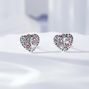 Détail macro de boucles d'oreilles cœur en argent S925 avec arbre de vie et fleurs rouges