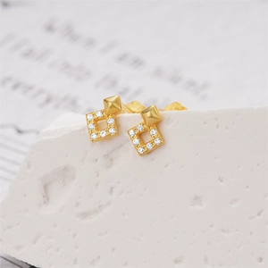 Makro-Detail goldener geometrischer Ohrstecker mit Pavé-Quadratsteinen auf Steingrund