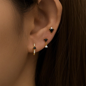 Detailed close-up of a model wearing a set of gold geometric onyx earrings with white diamonds