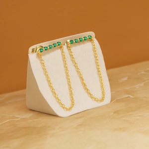 Detailed macro view of 18K gold chain earrings featuring vibrant green gemstones