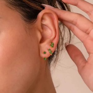 Detail of gold ear cuff and stud set featuring emerald green stones on model ear