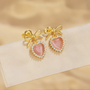 Dettaglio degli orecchini a fiocco dorato con pietra a cuore rosa e bordo in zirconi bianchi