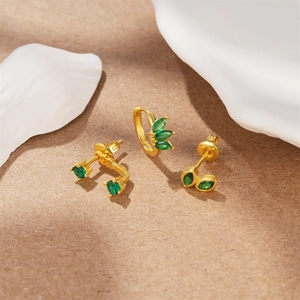 Detailed shot of gold earrings set with emerald green stones on textured surface