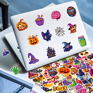 Close-up of assorted waterproof Halloween stickers on a white laptop lid and stack