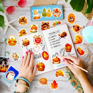 Flat lay of hands decorating a notebook with colorful Thanksgiving turkey and pumpkin stickers
