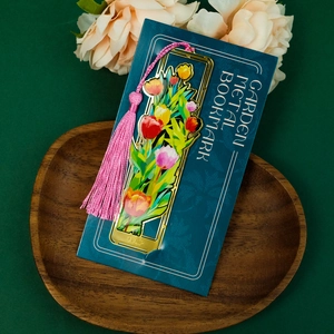 Detailed view of a golden brass hollow tulip bookmark with a vibrant pink tassel pendant
