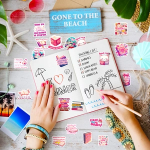 Flat lay of pink aesthetic reading stickers with beach props on white wooden desk