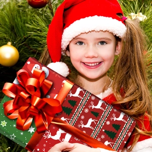 Girl holding a large Christmas gift box with reindeer patterns by a decorated tree