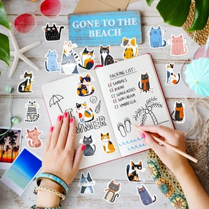 Flat lay of artistic waterproof cat stickers on a notebook with summer beach accessories