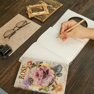 Vintage floral rose hardcover journal on dark wood desk with classic writing accessories