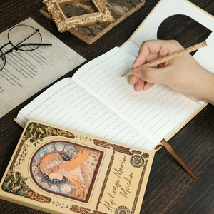 Detail of Alphonse Mucha art notebook with lined pages and silk bookmark on a wooden desk