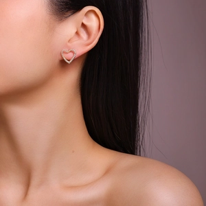 Macro view of gold heart-shaped stud earrings with sparkling pave-set stones worn by a model