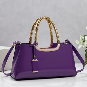 Detail of purple patent leather handbag with gold textured handle and adjustable strap
