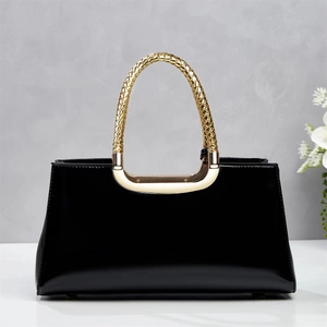 Detail of glossy black patent leather handbag featuring a textured gold metal handle