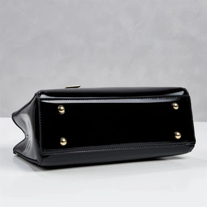 Close-up of black patent leather handbag base with four protective gold metal feet
