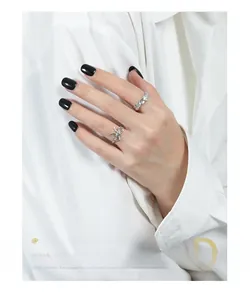 Close-up of minimalist silver bow ring and textured lava band set on model's hand