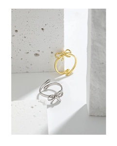 Detailed view of minimalist bow rings in gold and silver finish on stone texture