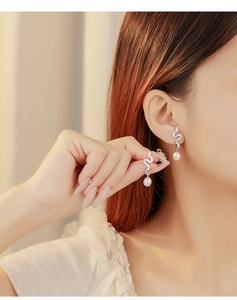 Close-up of a silver snake-shaped earring with zircon pavé and a teardrop pearl on model