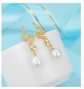Macro view of gold snake stud earrings with green gemstone eyes and hanging pearl