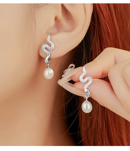 Macro shot of silver snake earrings with white pearls and sparkling micro-inlaid stones