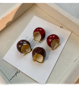 Close-up of retro dark red enamel bean stud earrings with polished gold-plated finish