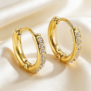 Detailed close-up of gold huggie earrings with cubic zirconia on silk fabric