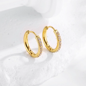 Detailed close-up of golden huggie earrings with cubic zirconia on white stone