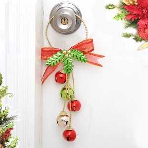 Colgante navideño de campanas con lazo rojo y hojas metálicas en el pomo de una puerta