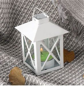 Weiße Metalllaterne mit brennender Kerze auf grauer Strickdecke und Herbstblättern