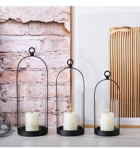 Three-piece black metal candle holders with glass covers and white classic candles