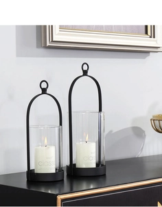 Set of two black metal candle holders with glass covers and white pillar candles on a side table