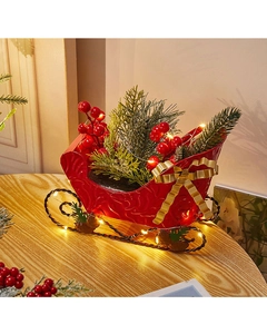 Close-up of red Christmas sleigh decor with golden bow, berries and LED lights