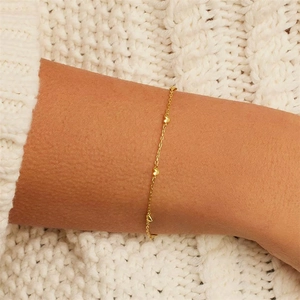 Close-up of minimalist gold heart charm bracelet worn over a white knit sweater
