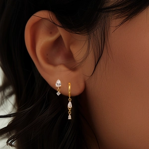 Close-up of golden hoop earrings and studs with sparkling teardrop-shaped zircons on model