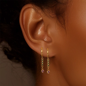 Close-up of elegant gold earrings with green and pink stone pendants on model