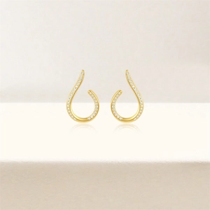 Macro detail of asymmetric gold drop earrings with micro-pave white crystals