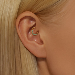 Macro shot of gold daith piercing ring with turquoise stones on ear cartilage