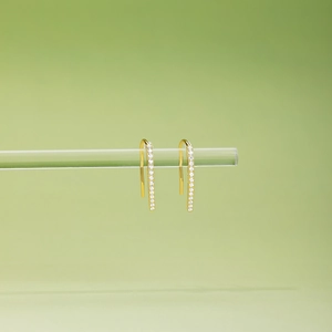 Detail of gold U-shaped drop earrings with micro-paved white zircons on a clear rod