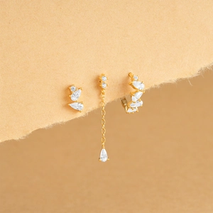 Detail of three gold S925 silver flower earrings with white zircon on torn paper edge