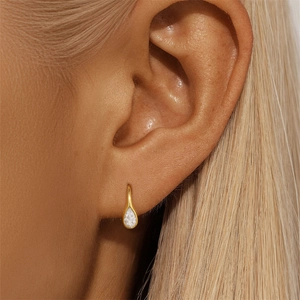 Close-up of elegant gold drop earrings with clear gemstone worn by a model on the ear
