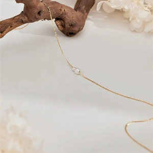 Detalle de dos perlas en cadena dorada minimalista con fondo floral elegante y zen