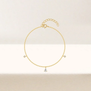 Dettaglio di un bracciale minimalista in oro con pietra a goccia e gemme delicate