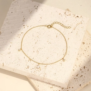 Dettaglio di un bracciale dorato con ciondoli a goccia su espositore in pietra naturale