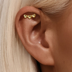 Close-up of golden polished triple heart helix piercing studs on upper ear cartilage