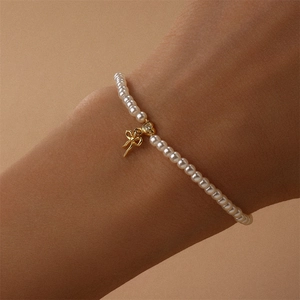 Detail eines Perlenarmbands mit goldenem Schleifenanhänger und Zirkon am Handgelenk