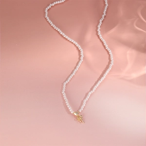 Detail der s925 Silber-Perlenkette mit goldenem Schleifenanhänger auf rosa Hintergrund