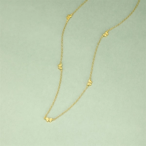 Détail d'un collier chaîne dorée avec petits pendentifs nœuds sur fond vert pastel doux