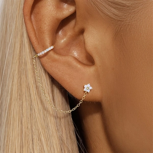 Macro shot of gold earring cuff with white flower stud and delicate chain on ear